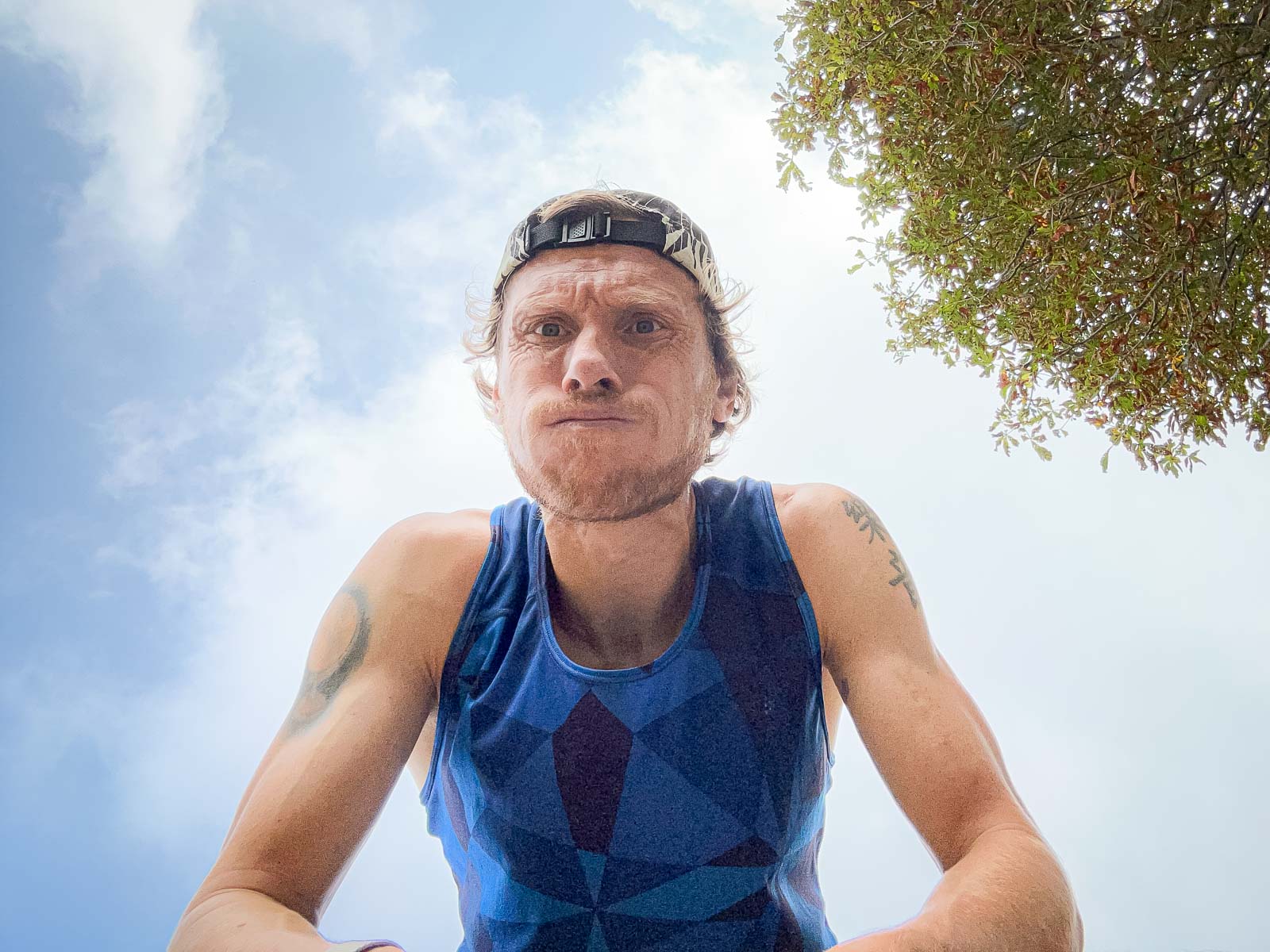 Läufer nach dem Training – Erschöpfung und Erfolg nach dem Lauf. Nahaufnahme eines Läufers, der nach einem Lauf schwer atmet. Er trägt ein blaues Trikot und eine Kappe, während er in die Kamera schaut.