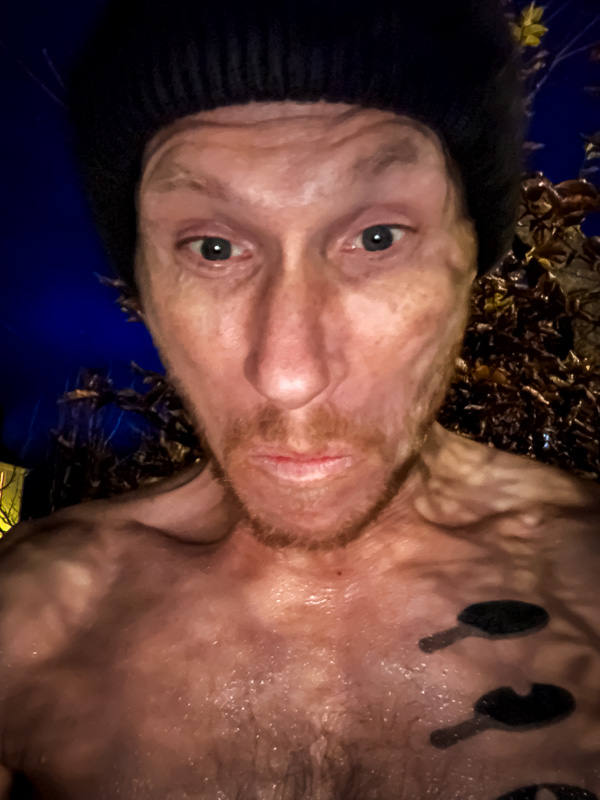 Ab ins kalte Wasser: Wenn der Eisbaden-Blick ernster wird, ist das Wasser unter 5 Grad.! Ein Mann mit schwarzer Mütze und nassem Oberkörper schaut mit angespannter Miene direkt in die Kamera. Der Hintergrund zeigt herbstliches Laub bei dunklem Abendhimmel.