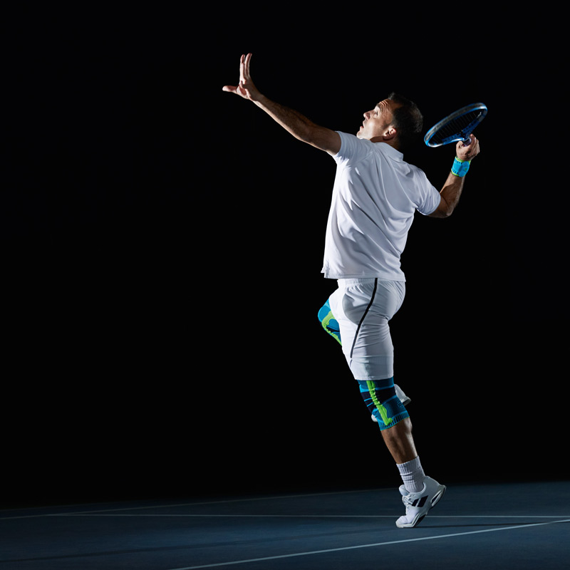 Tennisspieler in weißer Kleidung vor schwarzem Hintergrund beim Aufschlag