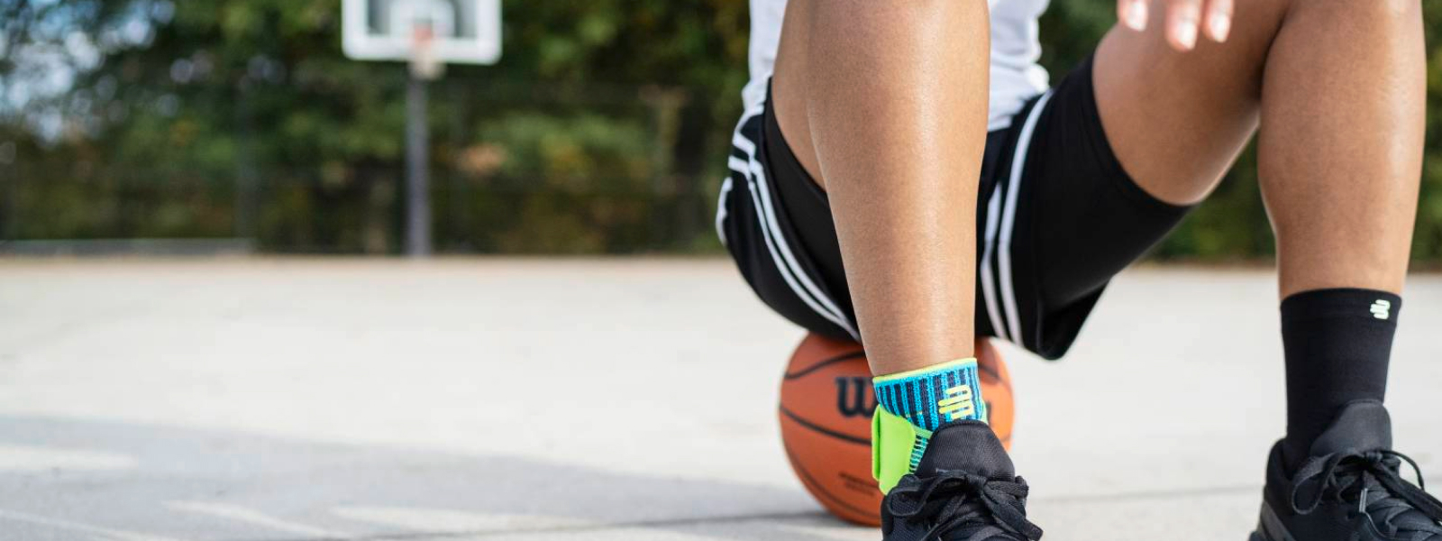 Streetball-Spieler mit Fußbandage sitzt auf einem Basketball auf einem Streetcourt-Feld