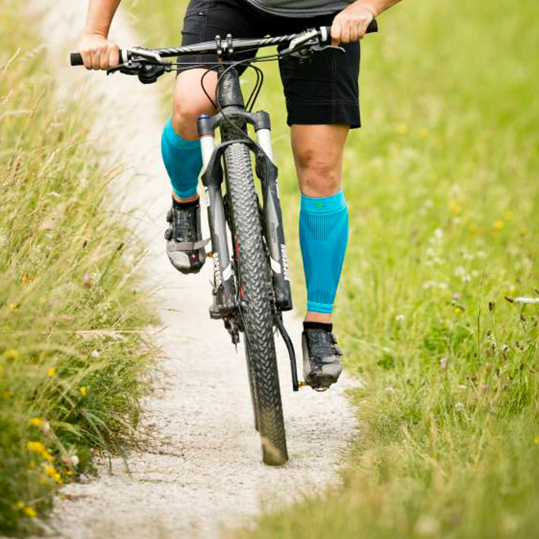 Frontalaufnahme Radfahrerin trägt Waden-Sleeves beim Fahren über einen Kiesweg auf dem Mountainbike