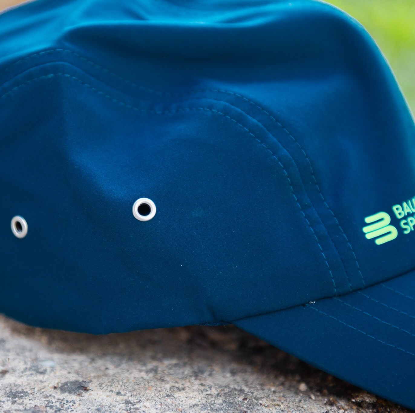 Detailaufnahme der blauen Bauerfeind Sports Cap mit seitlichen Metallösen, präzisen Nähten und angeschnittenem grünem Logo auf dem Frontpanel – ein sportliches Accessoire für Training, Tour und Alltag.
