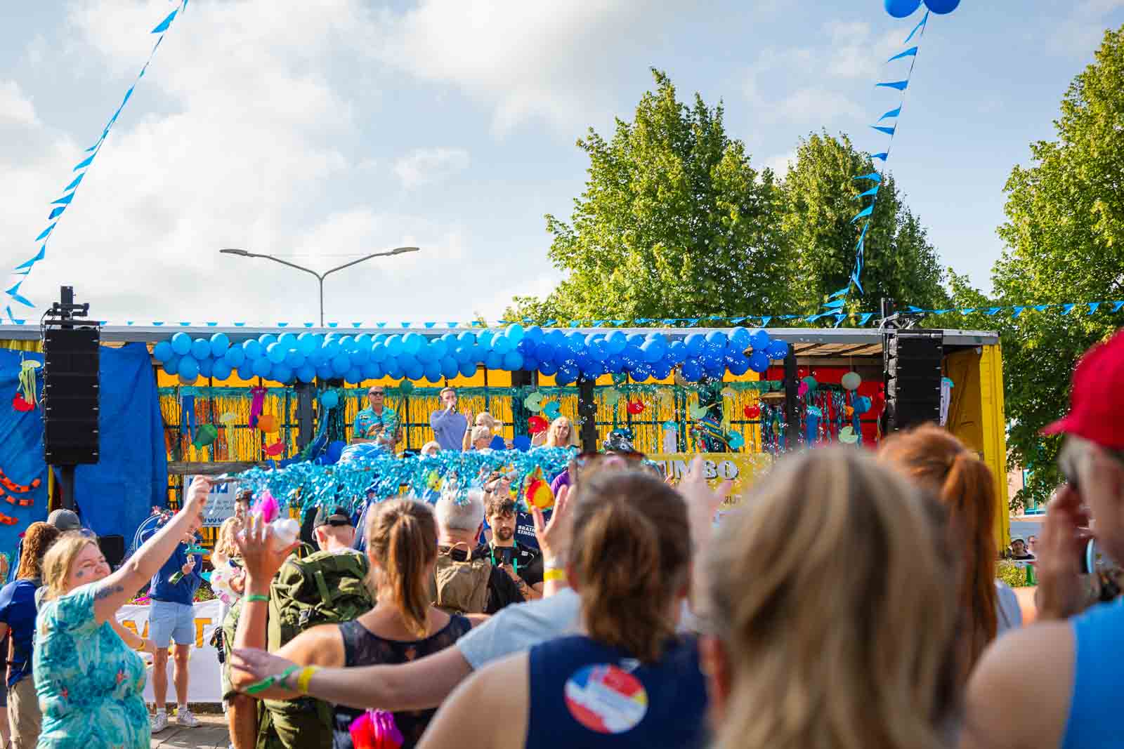 Bunt geschmückter Wagen mit blauen Luftballons und Zuschauern beim 4Daagse in Nijmegen, die den vorbeiziehenden Wanderern zujubeln.