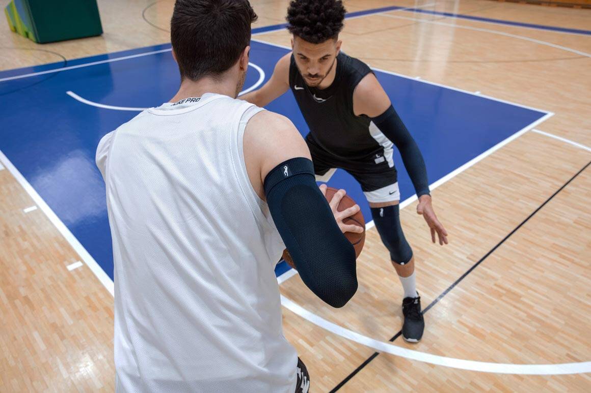 zwei Baskettballspieler spielen um einen Ball und tragen Armsleeve und Kniebandage