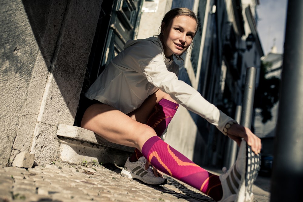 Läuferin mit lila Laufsocken dehnt sich auf einem Treppenabsatz sitzend