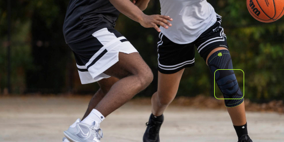 Zwei Basketballspieler auf einem Außenplatz im Spiel. Die im Vordergrund agierende Spielerin trägt eine schwarze Kniebandage und dribbelt den Ball, während sie von einem Gegenspieler verteidigt wird.