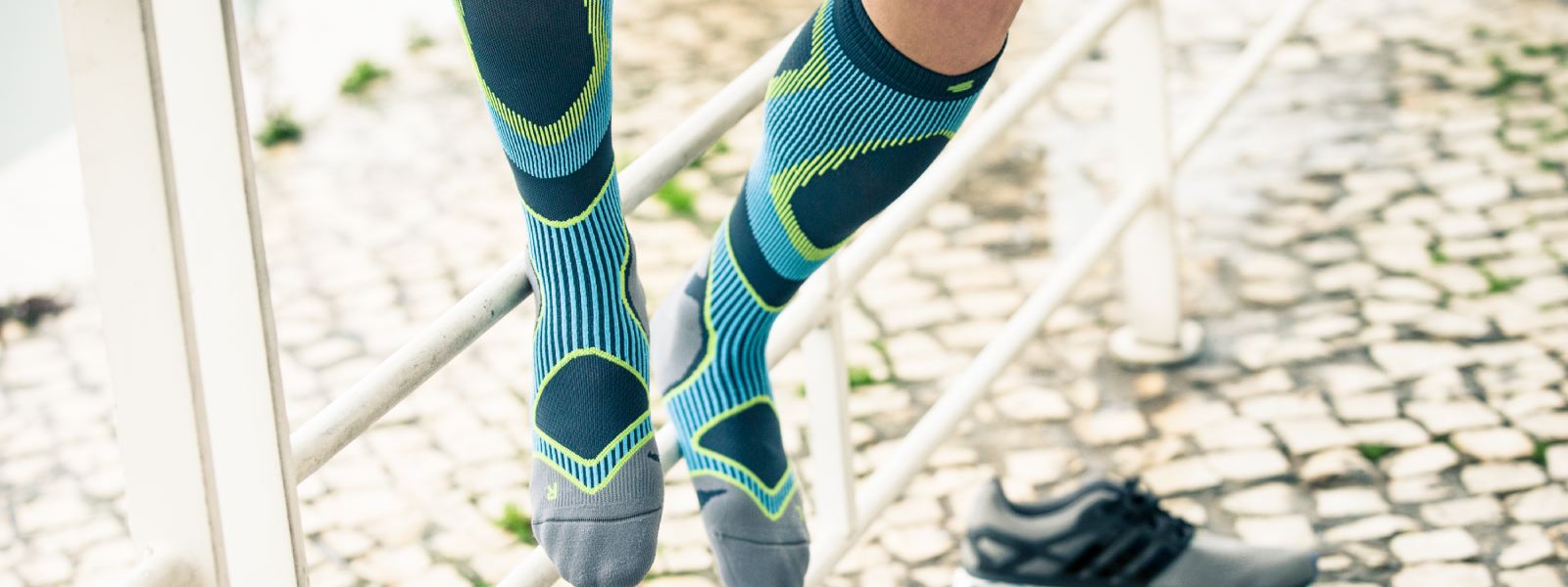 Mann mit blau-grauen Laufsocken sitzt auf einem Zaun und hat die Schuhe ausgezogen