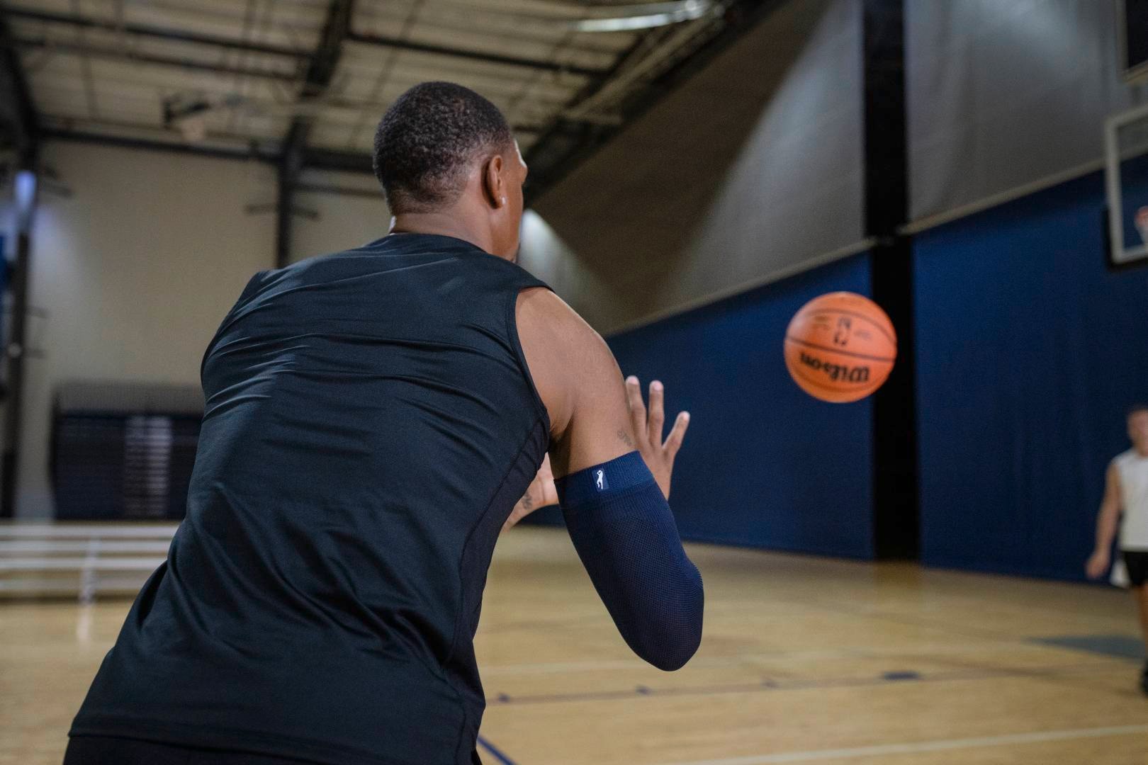 Basketballer mit blauem Armsleeve in Sporthalle erwartet einen Ball	 der ihm von einem anderen Spieler zugeworfen wird