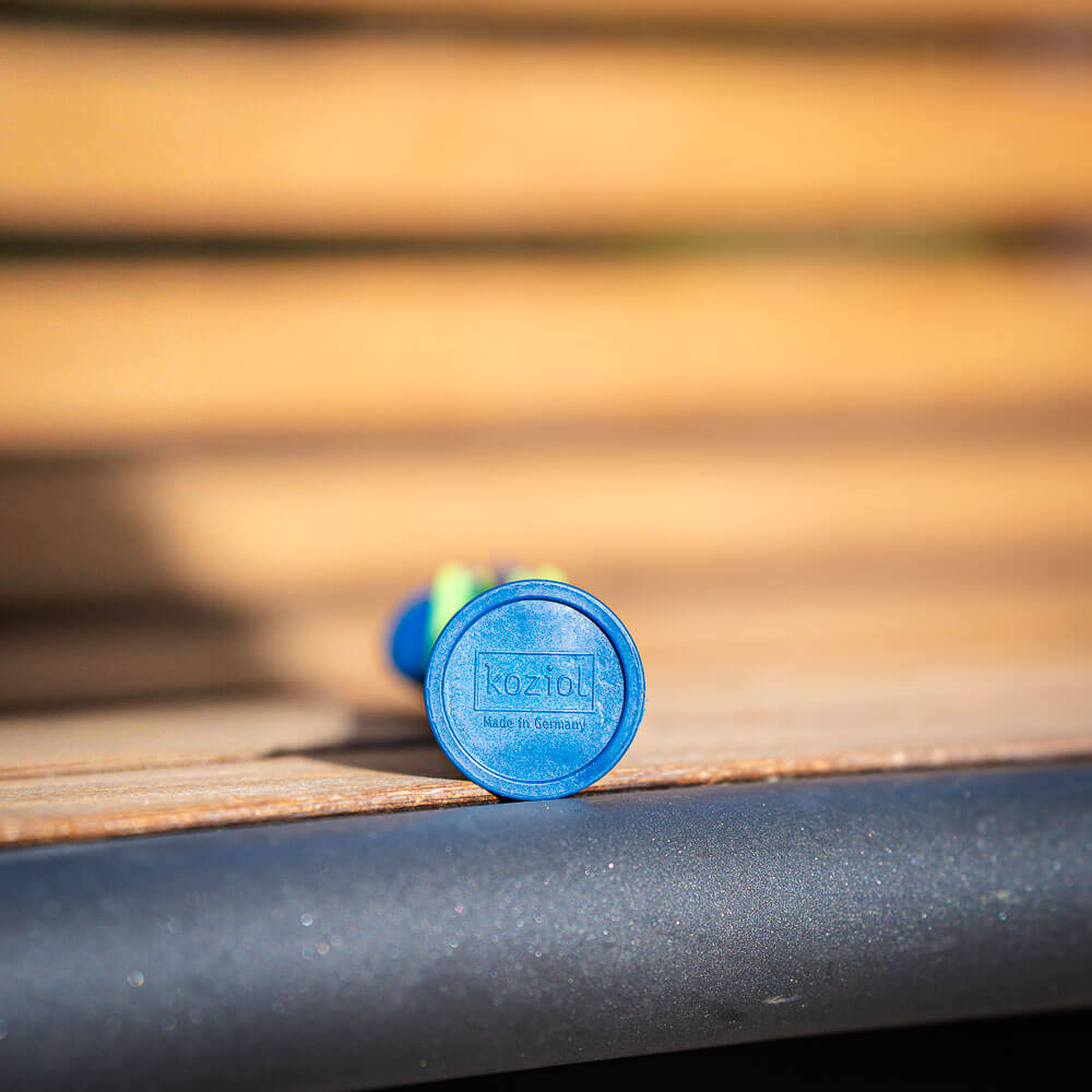 Made in Germany: Detailaufnahme eines nachhaltigen Bestecks Nahaufnahme der Unterseite eines blauen Bestecks, das auf einer Holzbank liegt. Auf dem Boden des Bestecks steht das Logo "Koziol Made in Germany".