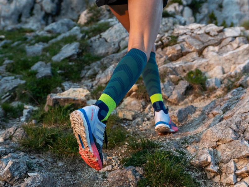 Trail Run Socks: Schutz vor Umknicken Läuferin läuft steinigen Bergabschnitt hoch und trägt Trail Run Socks