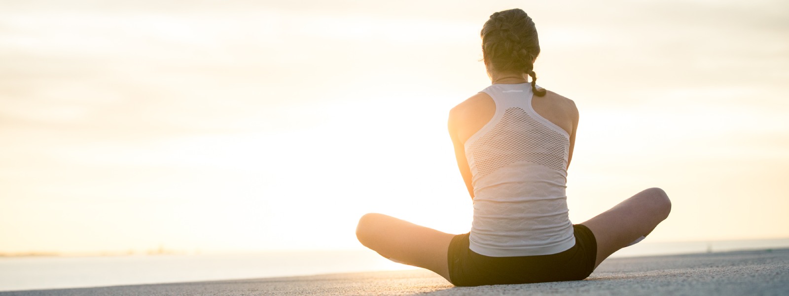 Durchatmen beim Laufen Läuferin sitzt im Schneidersitz in Richtung Sonne auf dem Boden