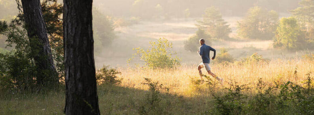 Mann joggt über eine Wiese	 im Vordergrund steht ein Baum	 im Hintergrund sind Hügel