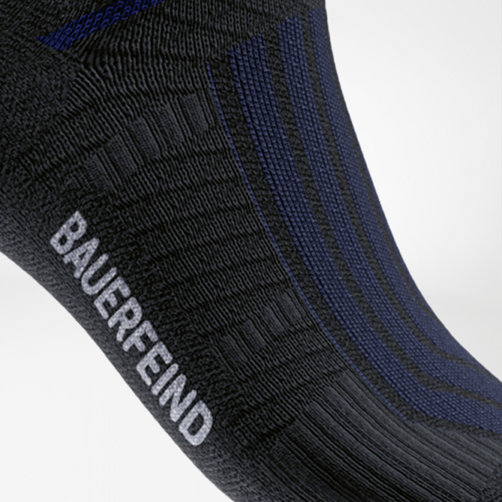Seitliche Detailaufnahme der schwarzen Run Performance Midcut Socke mit dezenten blauen Streifen und weißem „BAUERFEIND“-Schriftzug am Fuß.