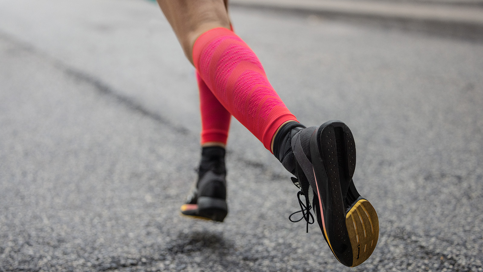 Flotter Blickfang: unsere Run Performance Compression Socks in pink Nahaufnahme: Lange pinke Laufsocken und schwarze Laufschuhe laufen über eine gepflasterte Straße in einer Stadt