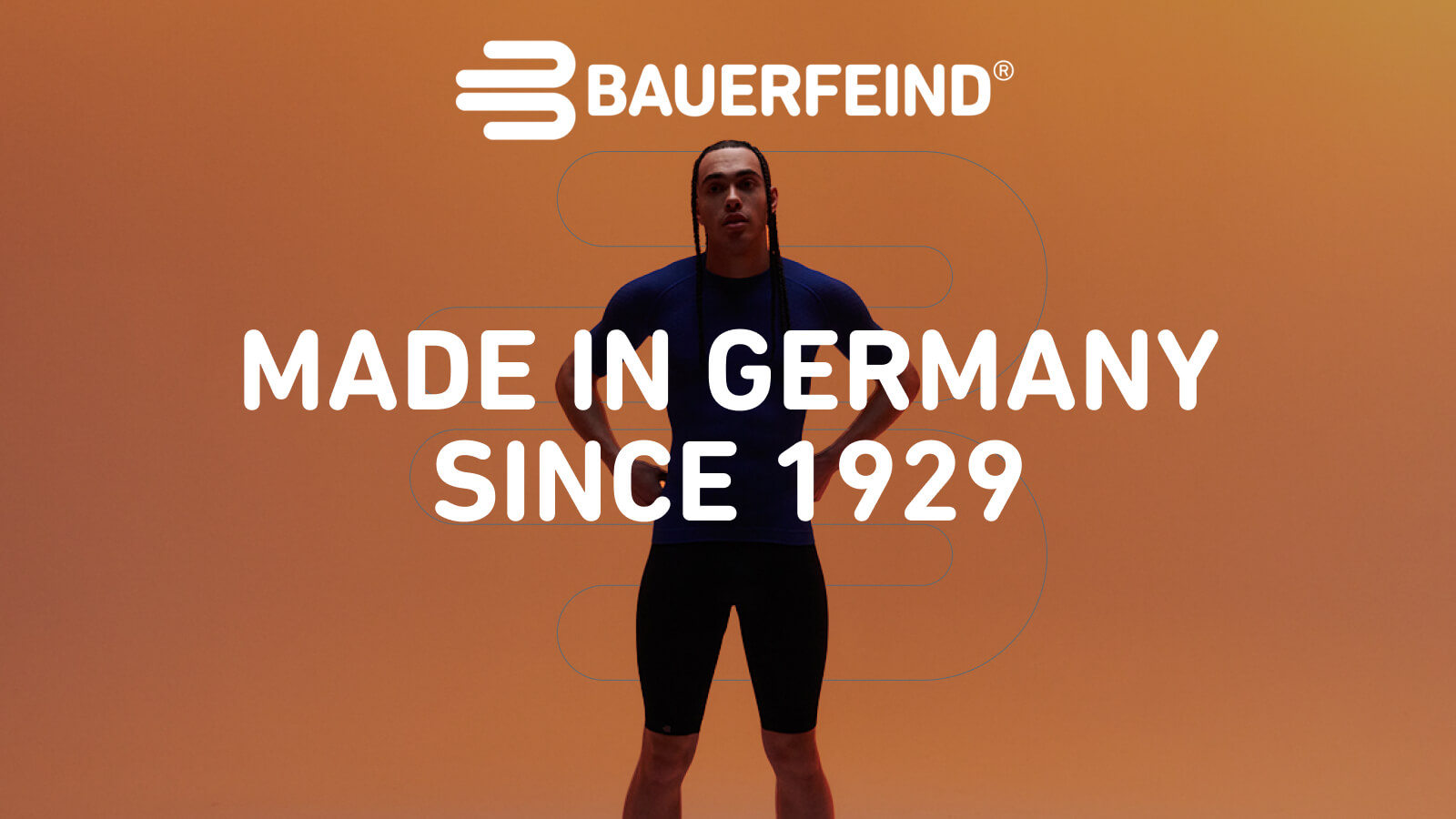 Selbstbewusst in Bauerfeind Kompressionskleidung Eine Person steht frontal mit leicht gespreizten Beinen vor einem orangefarbenen Hintergrund. Sie trägt ein eng anliegendes, blaues Funktionsshirt und eine schwarze Sporthose.