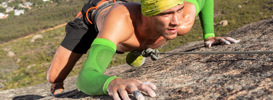 Kletterer am Felsen trägt grüne Kompressions-Sleeves für den Arm