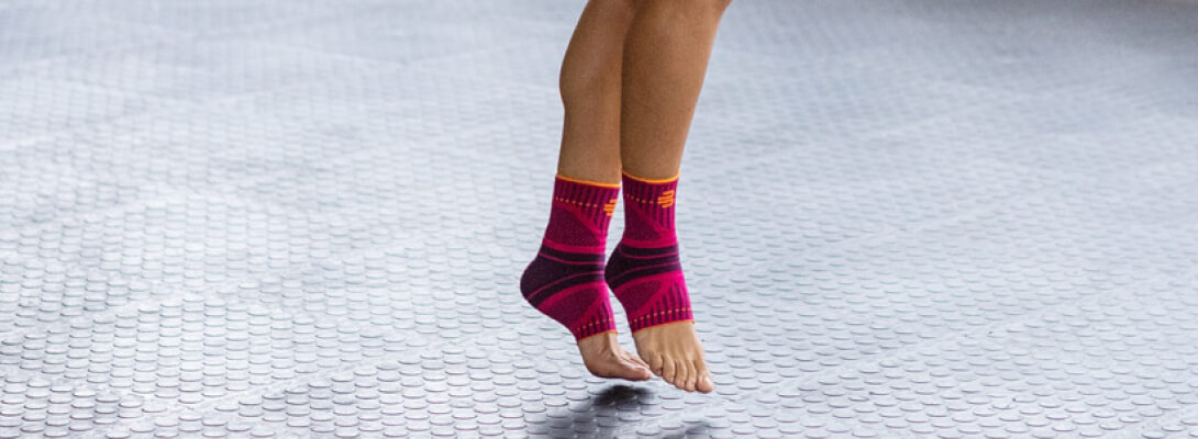Sprunggelenkbandage beim Seilspringen Zoom auf die Beine einer Frau die Sportbandagen für das Sprunggelenk trägt sie steht auf den Zehenspitzen auf einem grauen Untergrund