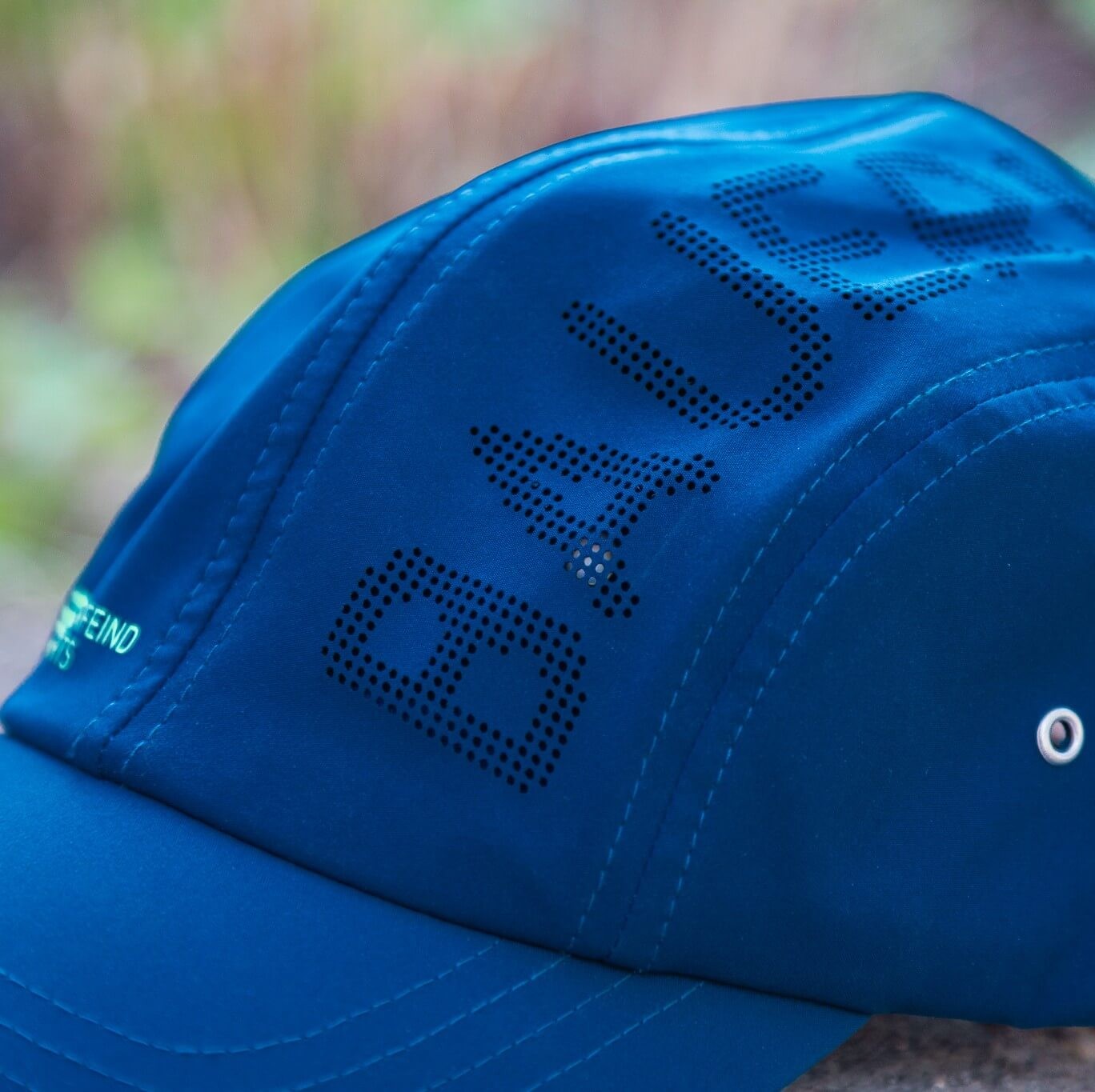 Nahaufnahme der blauen Bauerfeind Sports Cap mit perforierter BAUERFEIND-Schrift, sichtbaren Nähten, glatter Funktionsoberfläche und seitlicher Metallöse – sportliches Design mit Fokus auf Komfort und Belüftung.