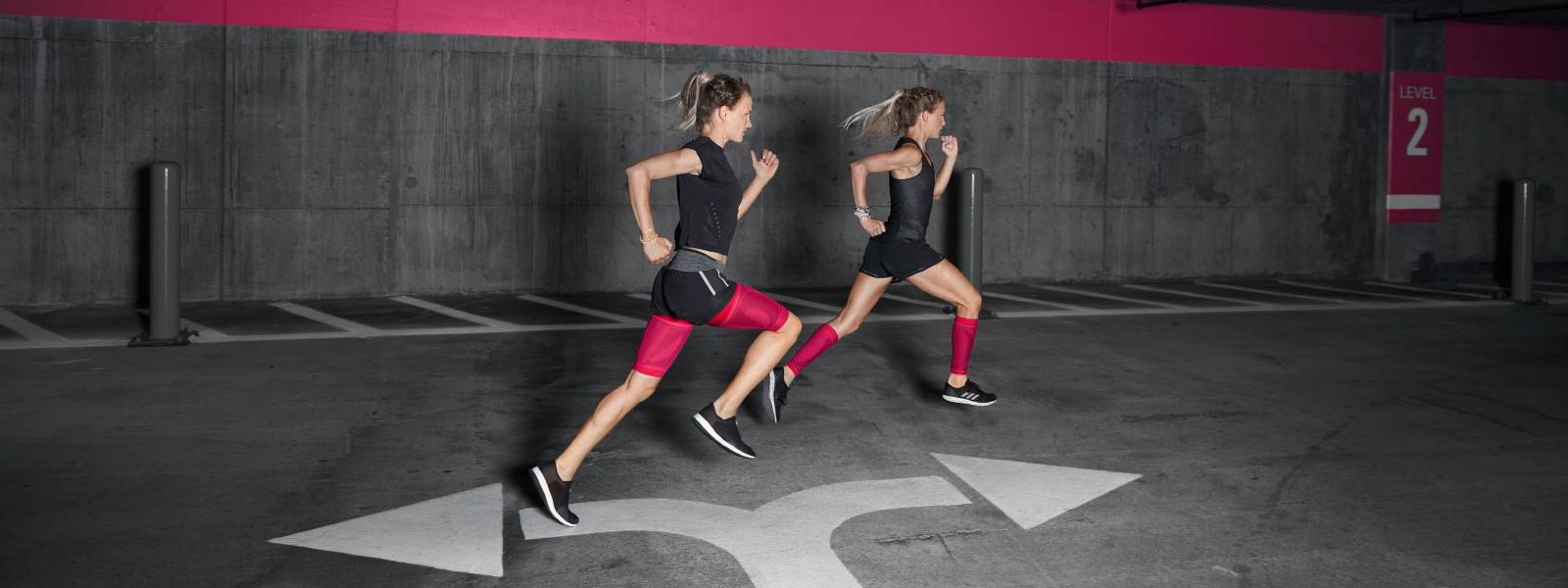 Zwei Läuferinnen mit pinken Compression Sleeves rennen durch ein Parkhaus