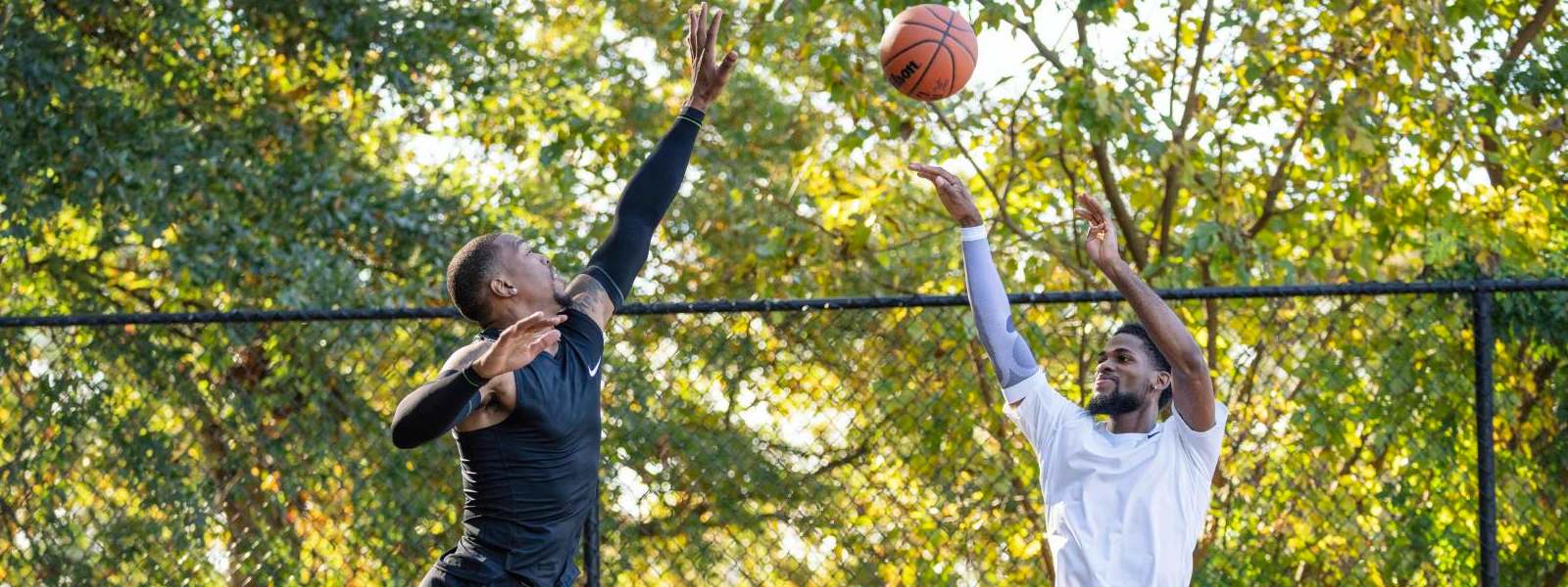 Basketballer in schwarzer Spielkleidung versucht Wurf seines Gegners in weißer Kleidung hoch über dem Boden zu blocken