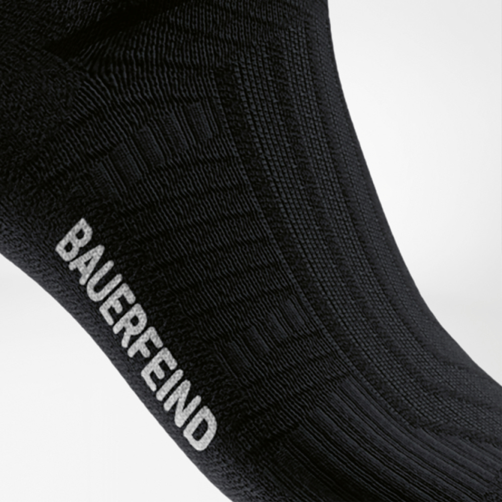 Stabilität im Tritt – Performance-Struktur mit BAUERFEIND-Qualität Nahaufnahme des Spannbereichs einer schwarzen Kompressions-Laufsocke mit eingestricktem BAUERFEIND-Logo und strukturierter Oberfläche für optimalen Halt.