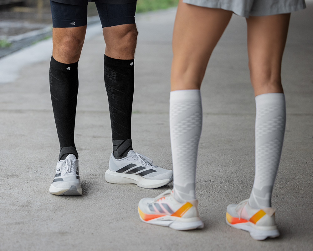 Froschperspektive: Läuferinnen mit lilafarbenen und weißen Laufsocken laufen durch eine belebte Stadt	 im Hintergrund Menschen	 Häuser und Laternen