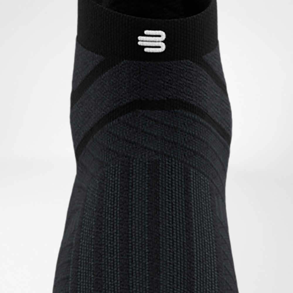 Schwarze Run Performance Low Cut Socke von Bauerfeind in Frontalansicht, die den Fußrücken mit eingearbeitetem Funktionsmuster und das elastische Bündchen mit weißem Logo zeigt.