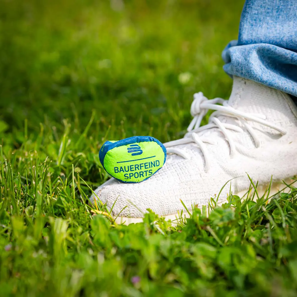 Kleiner Trainingsball auf Gras Kleiner Bauerfeind Sports Ball auf Gras, platziert neben einem weißen Schuh.