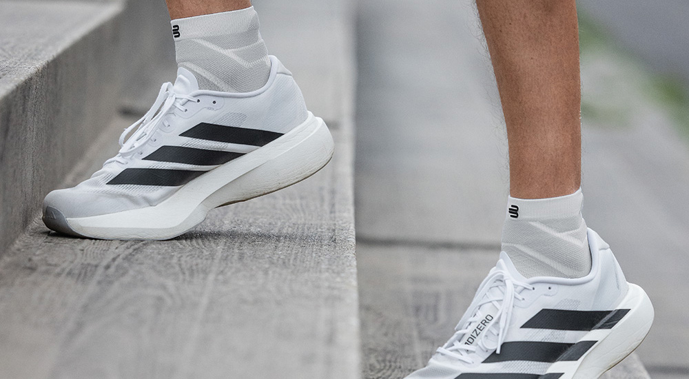 Schritt für Schritt nach oben Detailaufnahme von weißen Laufschuhen mit schwarzen Streifen und weißen Compression Socks, die beim Treppenlaufen getragen werden. Die Socken reichen über den Knöchel und bieten Halt und Komfort beim Training.