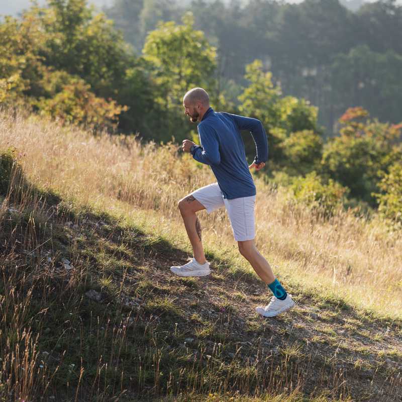 Mann rennt mit einer Achillessehnenbandage am Fuß einen Hügel mit Gras hinauf