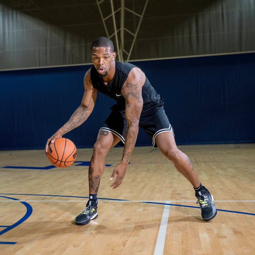 Ein Basketballspieler im schwarzen Outfit dribbelt auf dem Spielfeld. An seinen Knöcheln trägt er die Bauerfeind Sports Ankle Support in Schwarz.