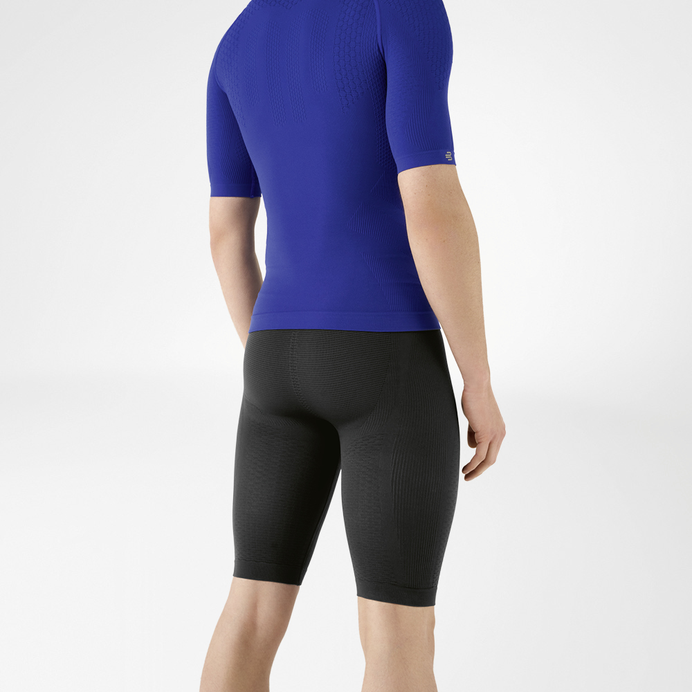 Der Mann trägt ein eng anliegendes, blaues Shirt, das seinen Oberkörper betont, sowie eine knielange, marineblaue, eng geschnittene Sporthose, die seinen Unterkörper umschließt.