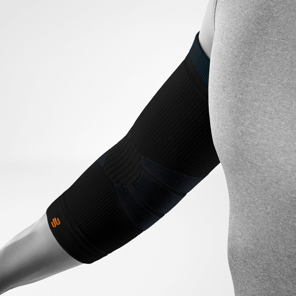 Schräg dargestellte schwarze Outdoor Compression Elbow Support am Unterarm und Ellenbogen. Die Bandage zeigt deutlich die anatomisch geformten Kompressionszonen sowie das integrierte Logo im unteren Bereich.