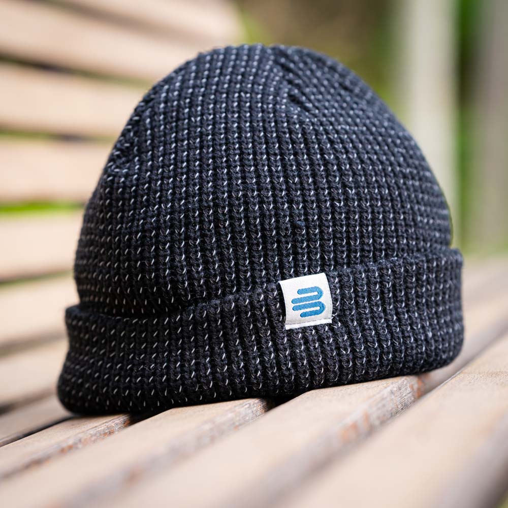 Stylisch im Freien: Die Bauerfeind Sports Mütze in Aktion Eine schwarze Bauerfeind Sports Strickmütze mit dem Logo auf einem Holzbank im Freien. Die grobe Strickstruktur sorgt für ein modernes, sportliches Aussehen.