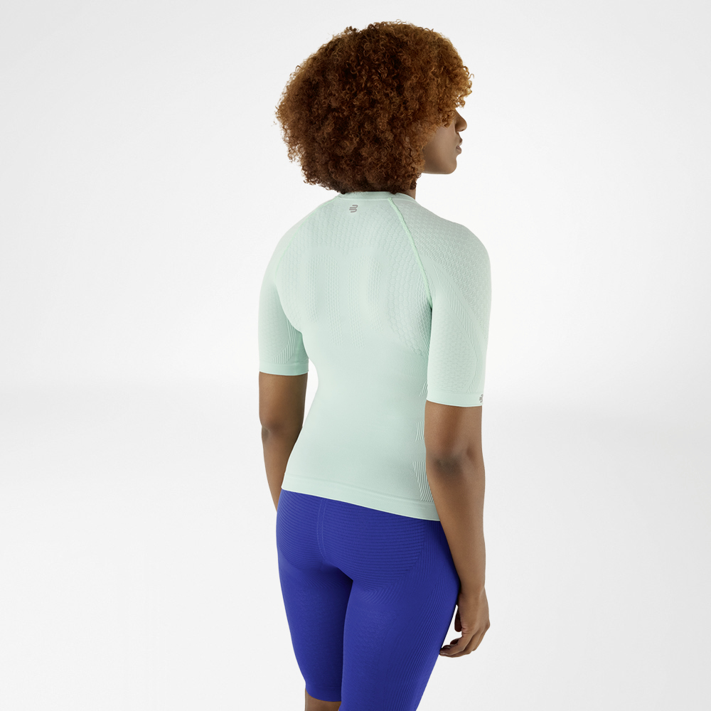 Rückansicht einer Frau mit lockigem Haar in einem mintgrünen Kompressionsshirt und blauen Leggings, die leicht zur Seite schaut.