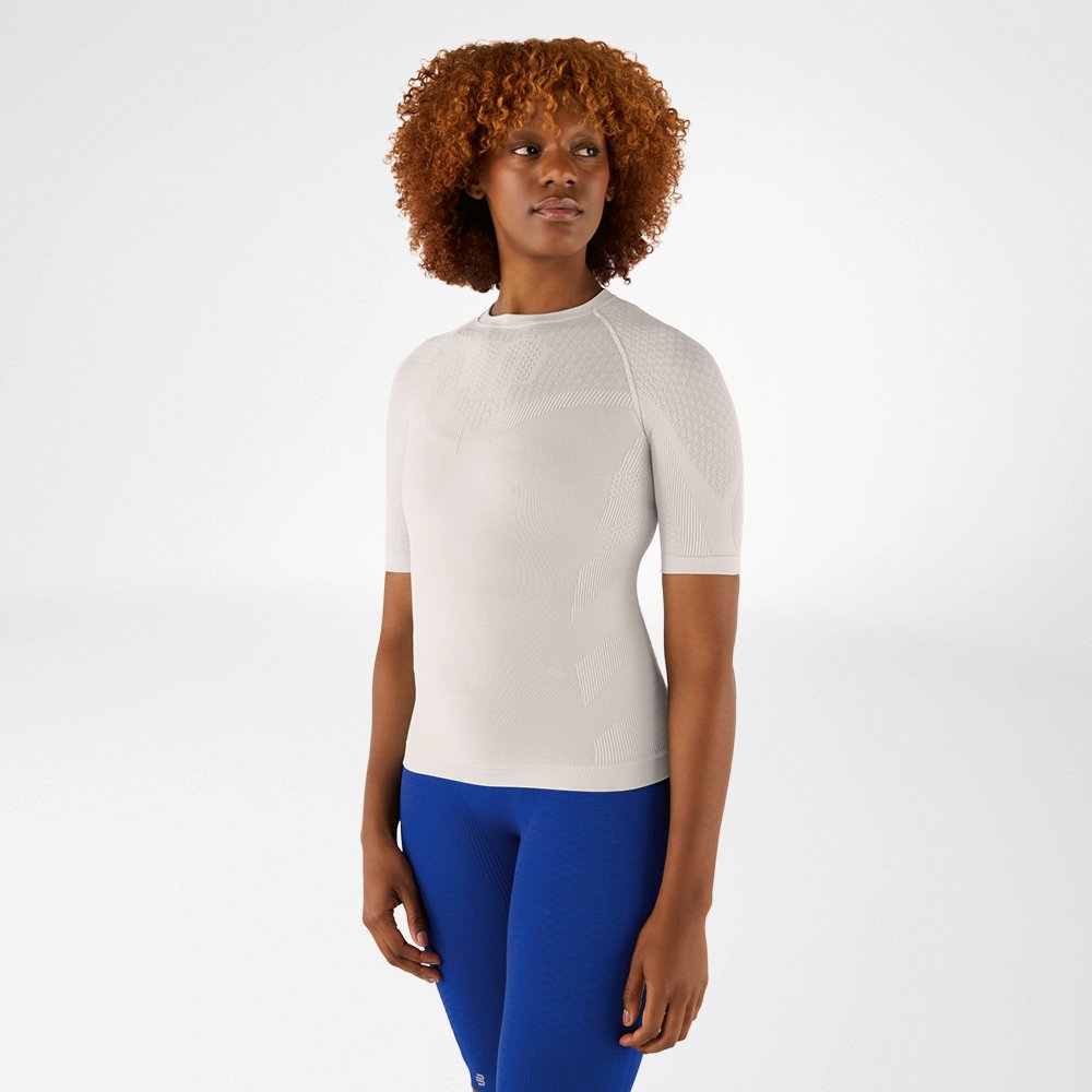 Frau mit lockigem Haar in einem silbergrauen Kompressionsshirt und blauen Leggings. Sie steht frontal und schaut zur Seite.