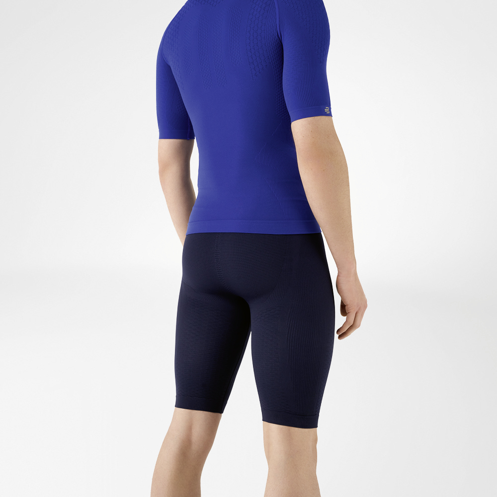 Der Mann trägt ein eng anliegendes, blaues Shirt, das seinen Oberkörper betont, sowie eine knielange, marineblaue, eng geschnittene Sporthose, die seinen Unterkörper umschließt.