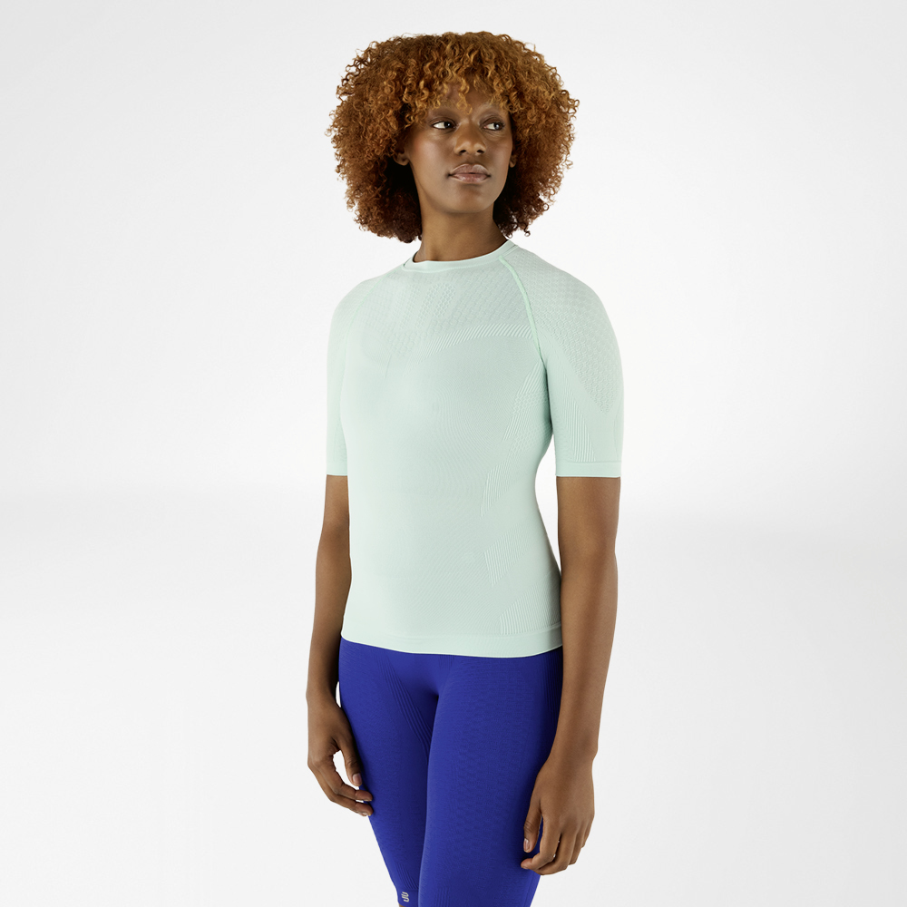Frau in einem mintgrünen Kompressionsshirt und blauen Leggings, frontal stehend.