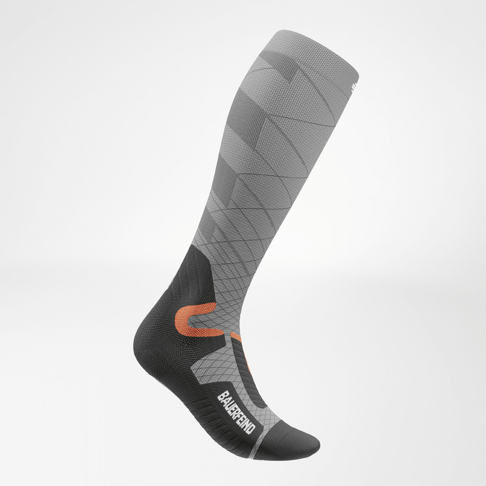 Seitenansicht der Kompressionsskisocke für Damen Kompressionsskisocke für Damen in Grau, Seitenansicht mit anatomisch optimierter Passform, sportlichem Design und kontrastierenden Details in Orange und Schwarz.