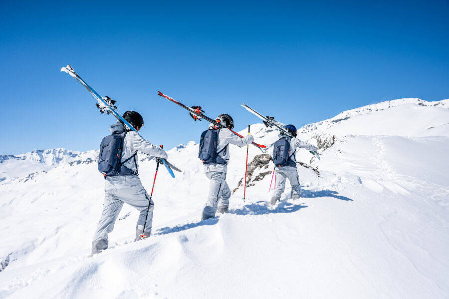 Drei Skifahrer tragen ihre Skier auf den Schultern durch tiefen Schnee einen Berg hinauf