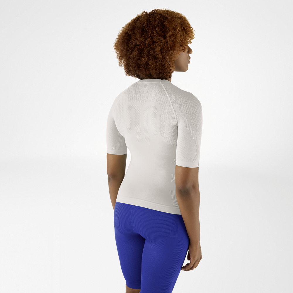 Rückansicht einer Frau mit lockigem Haar in einem athrazit farbenen Kompressionsshirt und blauen Leggings, die leicht zur Seite schaut.