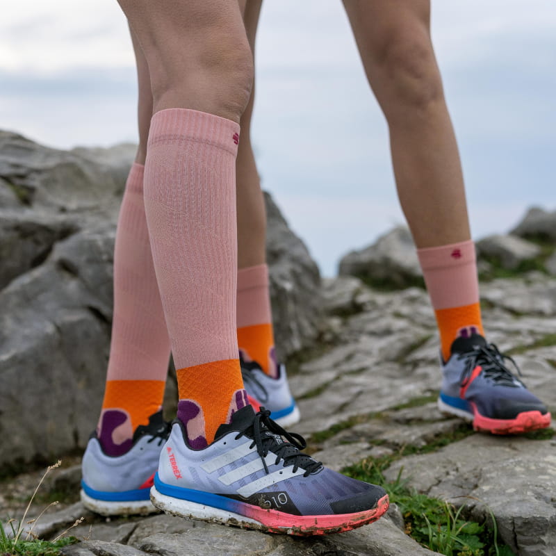 Trail Run Socken Peach Rosa Mittellange und Kompressionssocken der Trail Run Socke von Bauerfeind Sports auf einem Felsen