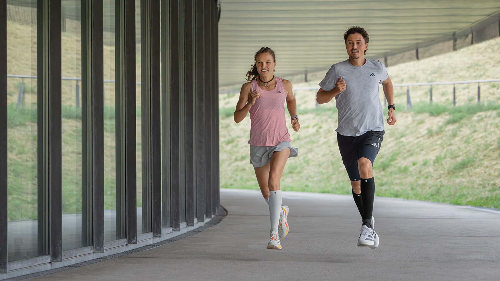 Gas geben und Spaß haben: mit unseren Run Perfomance Compression Socks Läuferin mit weiß-rosa Laufsocken läuft neben einer modernen Mauer