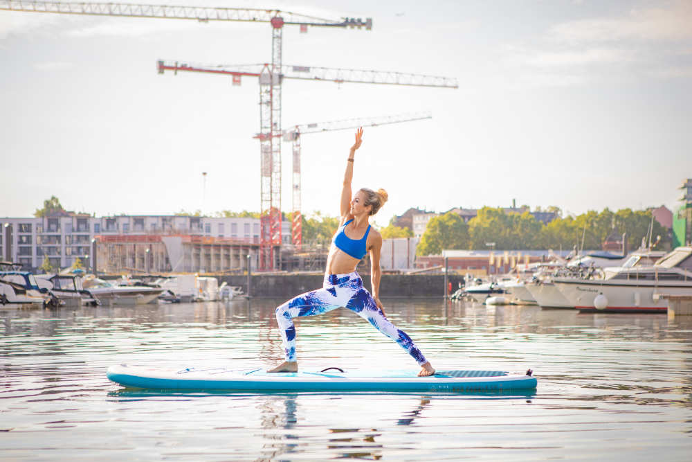 Frau macht Yoga auf einem Board mit Hafen im Hintergrund